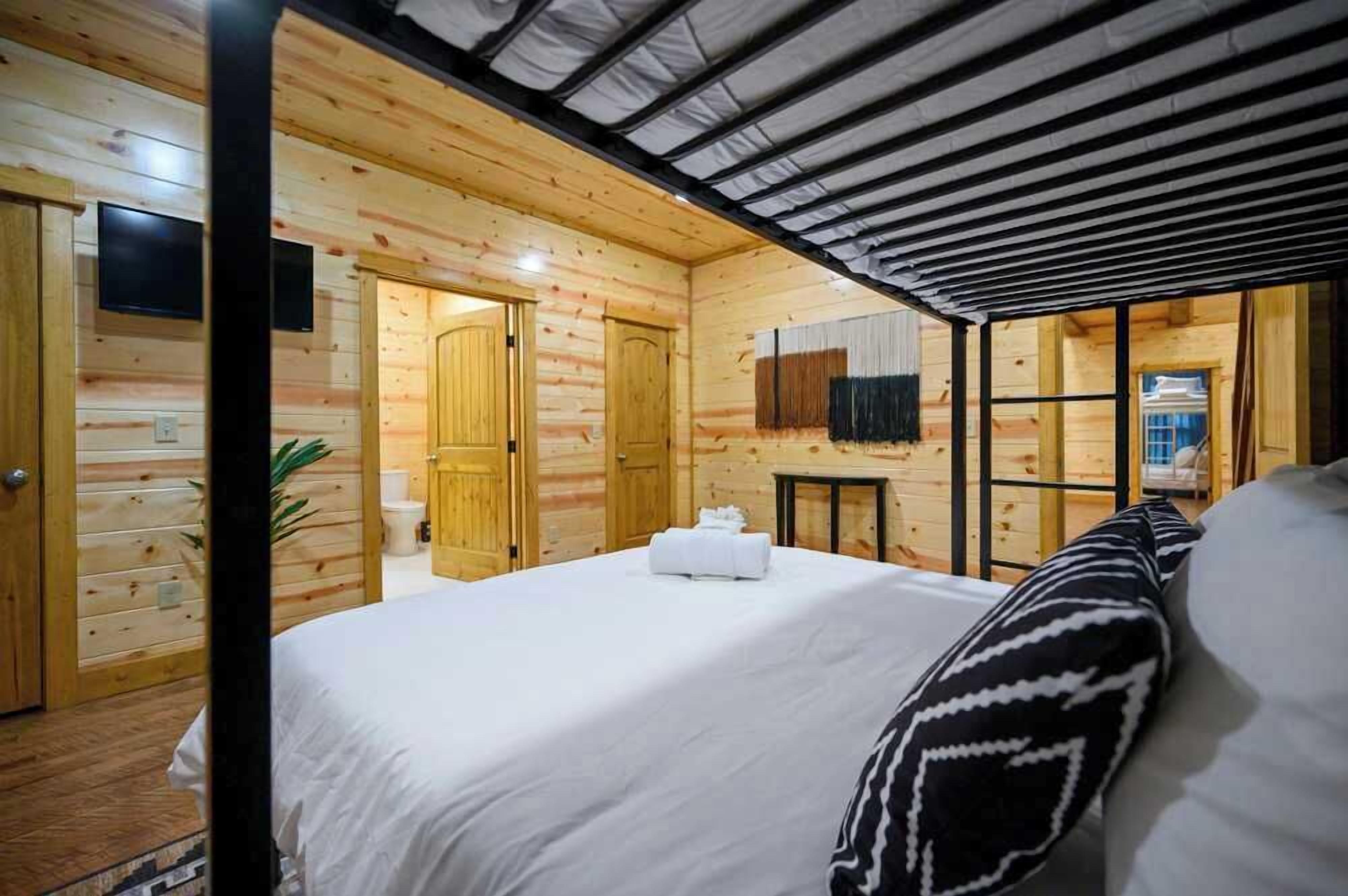 Une pièce aménagée comme un chalet en bois, avec un lit, une petite table et un téléviseur fixé au mur.