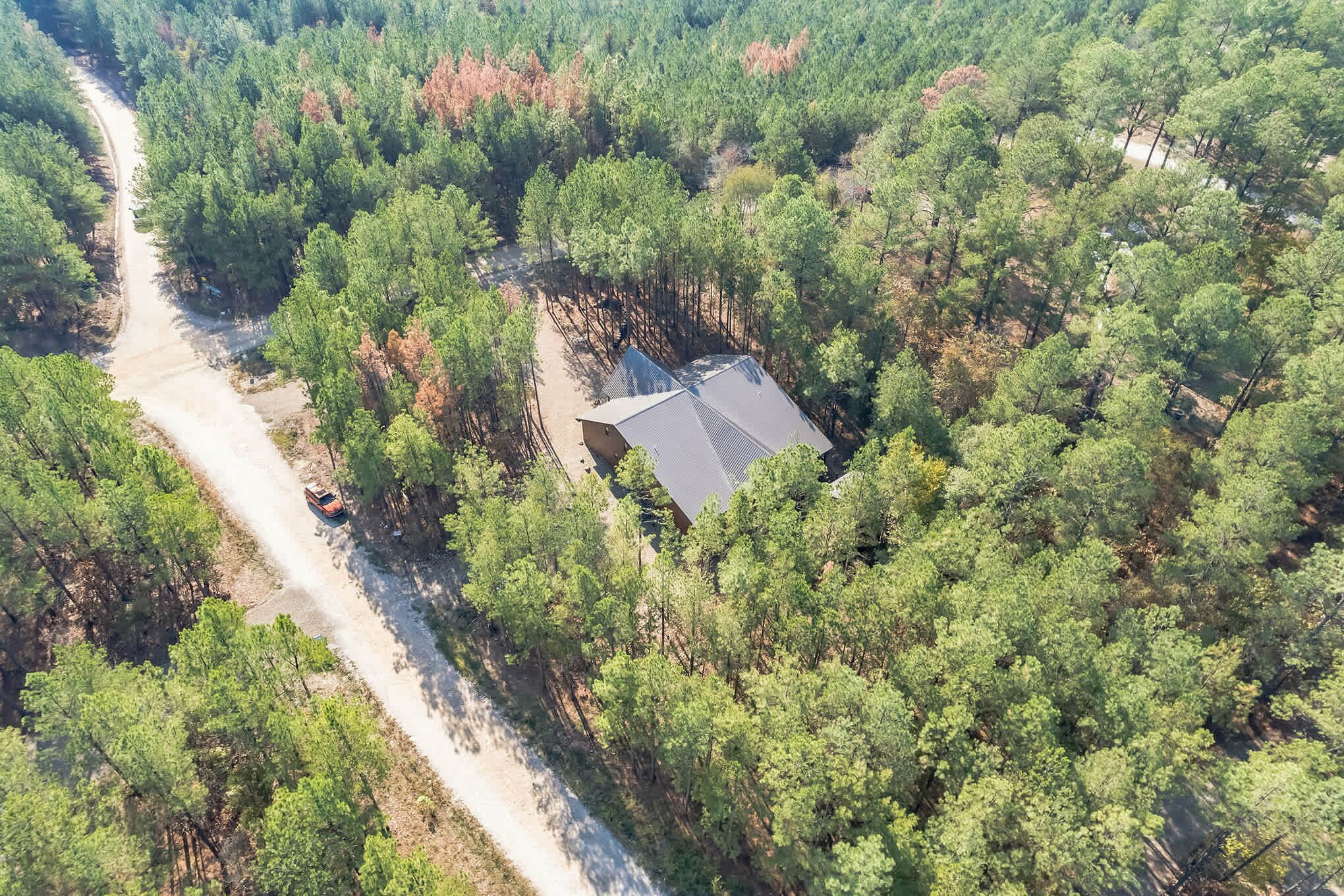An aerial view of a forested area with a single building featuring a sloped roof.