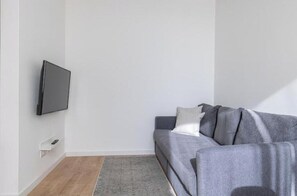 A room with a grey sofa, a flat-screen TV mounted on the wall, and a small white shelf. - Apartment with stunning views of the Tagus River and the Atlantic (Cruz Quebrada)
