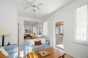 Ein geräumiges Wohnzimmer mit Deckenventilator, einem Karomuster-Sofa, einem Holztisch und einem Essbereich im Hintergrund.