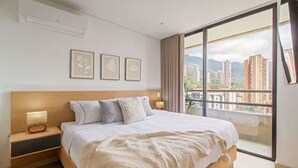Ein Schlafzimmer mit einem großen Bett, einem Nachttisch, einer Wand-Klimaanlage und einem Fenster mit Blick auf die Stadt.