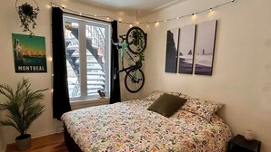 Et soveværelse med blomstret sengetæppe, en cykel hængende på væggen, en plakat af Montreal og en lyskæde.