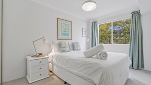 A bedroom with a bed, a bedside table, a lamp, and a window with curtains. - Yonder #5 - Walk to beach (Avoca Beach)