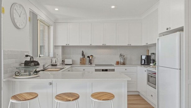 A modern kitchen with white cabinetry, a central island with stools, a coffee machine, and a refrigerator. - Yonder #5 - Walk to beach (Avoca Beach)