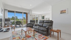 A modern living room with a leather sofa, a coffee table, and a dining area with a table and chairs. - Yonder #5 - Walk to beach (Avoca Beach)