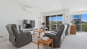 A modern living room with a flat-screen TV, leather sofas, a coffee table, and a balcony with a view. - Yonder #5 - Walk to beach (Avoca Beach)