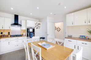 Une cuisine moderne avec des meubles blancs, une table à manger en bois et une hotte noire.