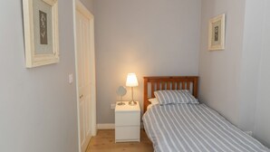 Ein kleines Schlafzimmer mit Bett, Nachttisch, Lampe und gerahmten Bildern an den Wänden.