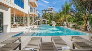A swimming pool with lounge chairs, a water slide, and a view of a modern building. - Pool, Spa & Rooftop Fire Pit • Steps to Beach (Siesta Key)