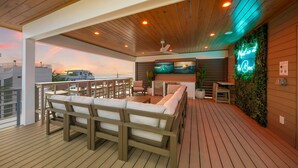 Eine Terrasse mit Holzmöbeln, einem Fernseher und einem Neonzeichen.