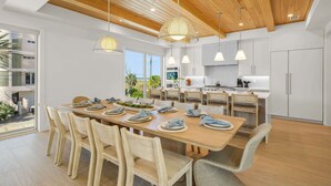 Eine moderne Küche mit weißen Schränken, ein Essbereich mit Holztischen und -stühlen und ein Blick ins Freie.