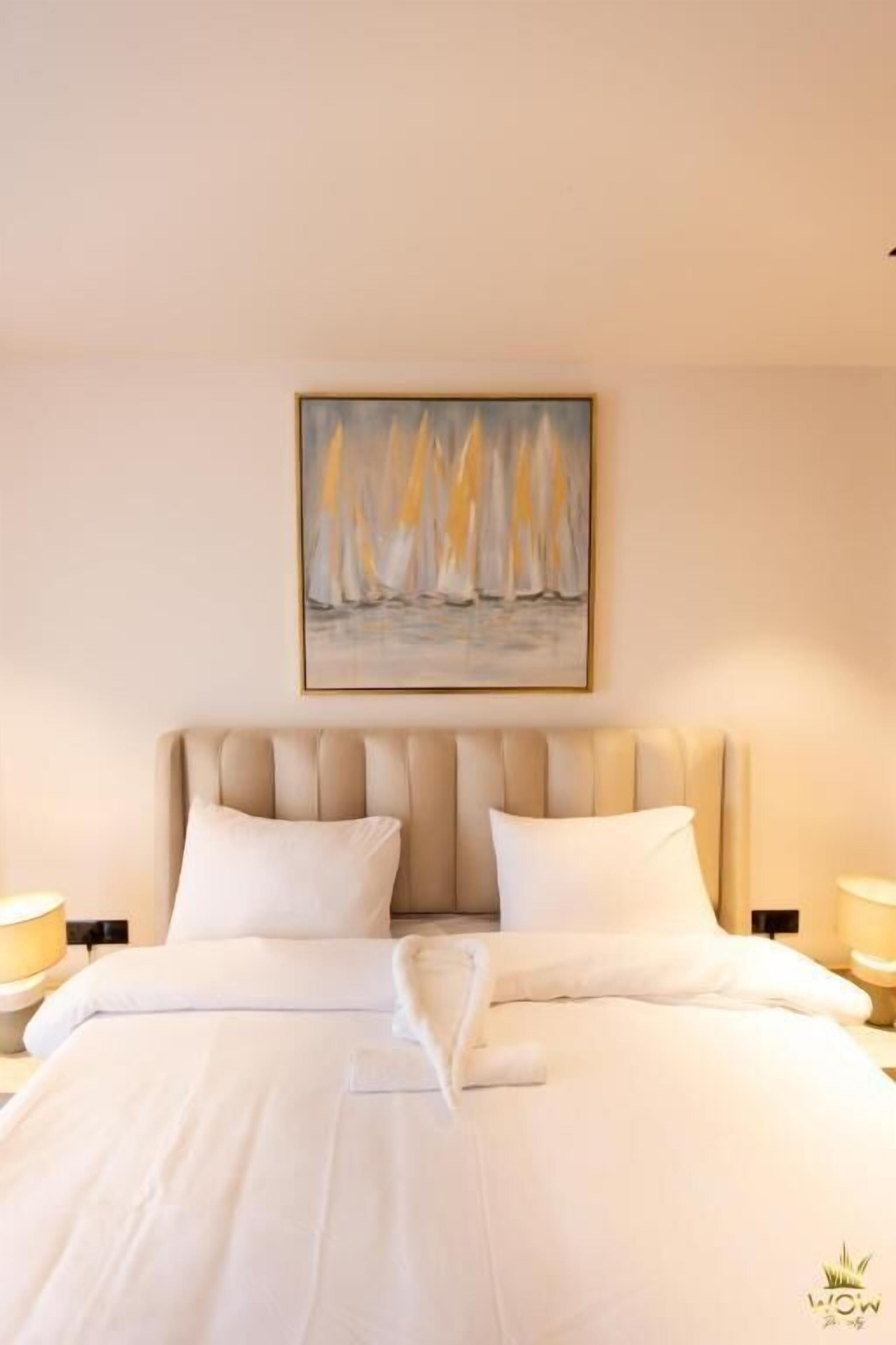 A hotel room with a large bed, a headboard, two bedside tables, and a painting on the wall.