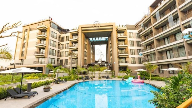 Un hotel moderno con piscina, mobiliario exterior y entrada central.
