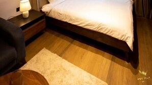 Un dormitorio con cama, mesitas de noche, lámpara, un cuadro y vistas a través de cortinas.