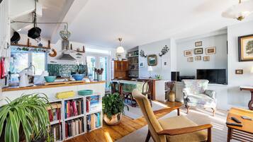 A spacious living area with a dining table, a comfortable armchair, and a bookshelf filled with books.