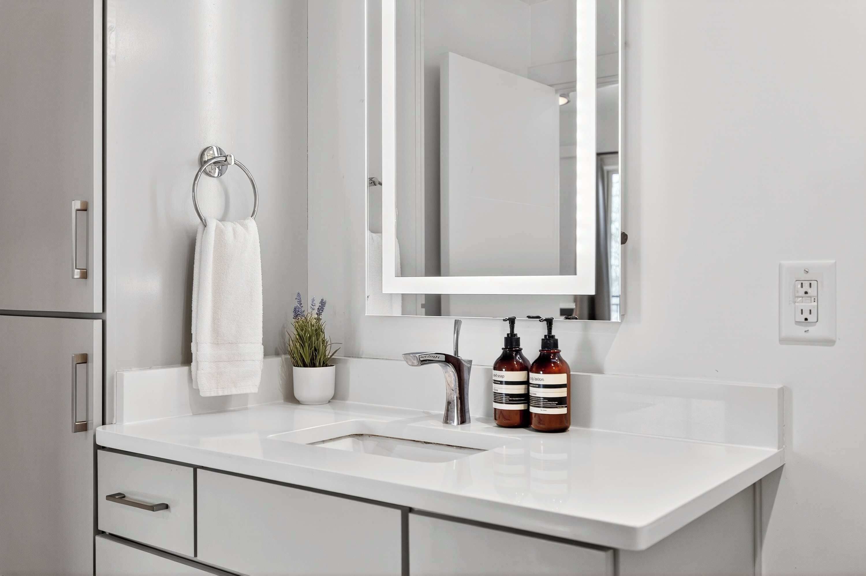 A modern bathroom with a white sink, a mirror, a towel ring, and two bottles of shampoo.