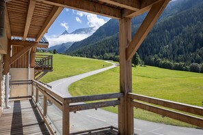 Eine Holzhütte mit Blick auf eine kurvenreiche Straße durch ein grünes Tal und Berge.