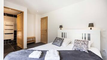 A hotel room with a bed, two bedside lamps, a wooden wardrobe, and a bench.
