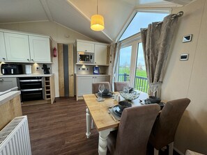 A compact kitchen with a microwave, oven, and dining area with a table set for two. - The Vogue Lodge - Golden Anchor Holiday Park (LM1) (Chapel Saint Leonards)