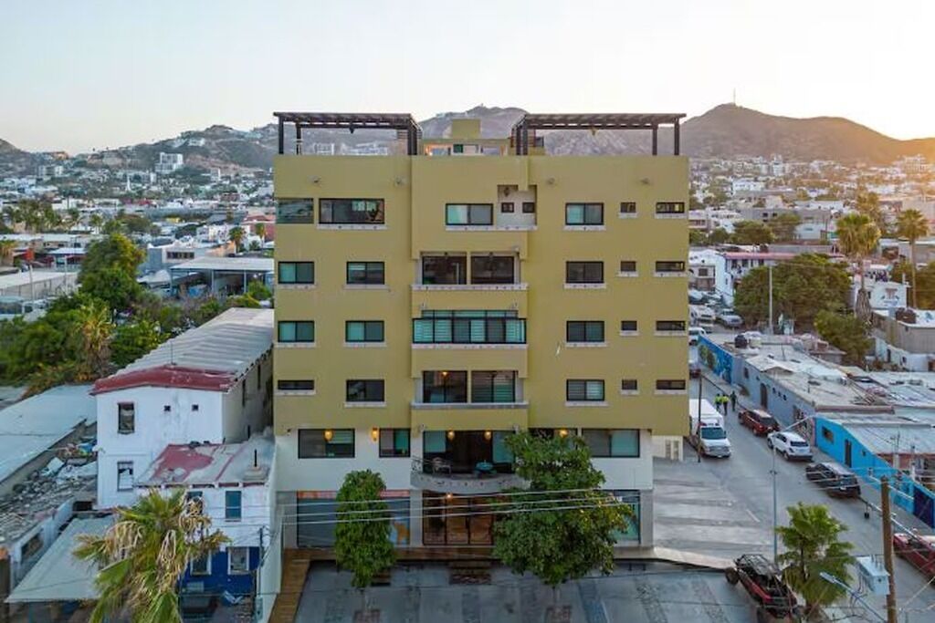 Um hotel com vários andares, varandas, área de estacionamento e vista para a paisagem urbana ao redor.