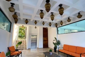 A lobby with a modern ceiling design, a seating area with orange sofas, and a large window. - Lugar hermoso, cómodo y céntrico. ¿Algo más? (Cabo San Lucas)