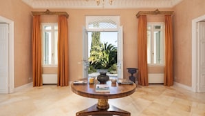Quarto com uma mesa redonda, um candelabro e vista através de uma porta aberta.