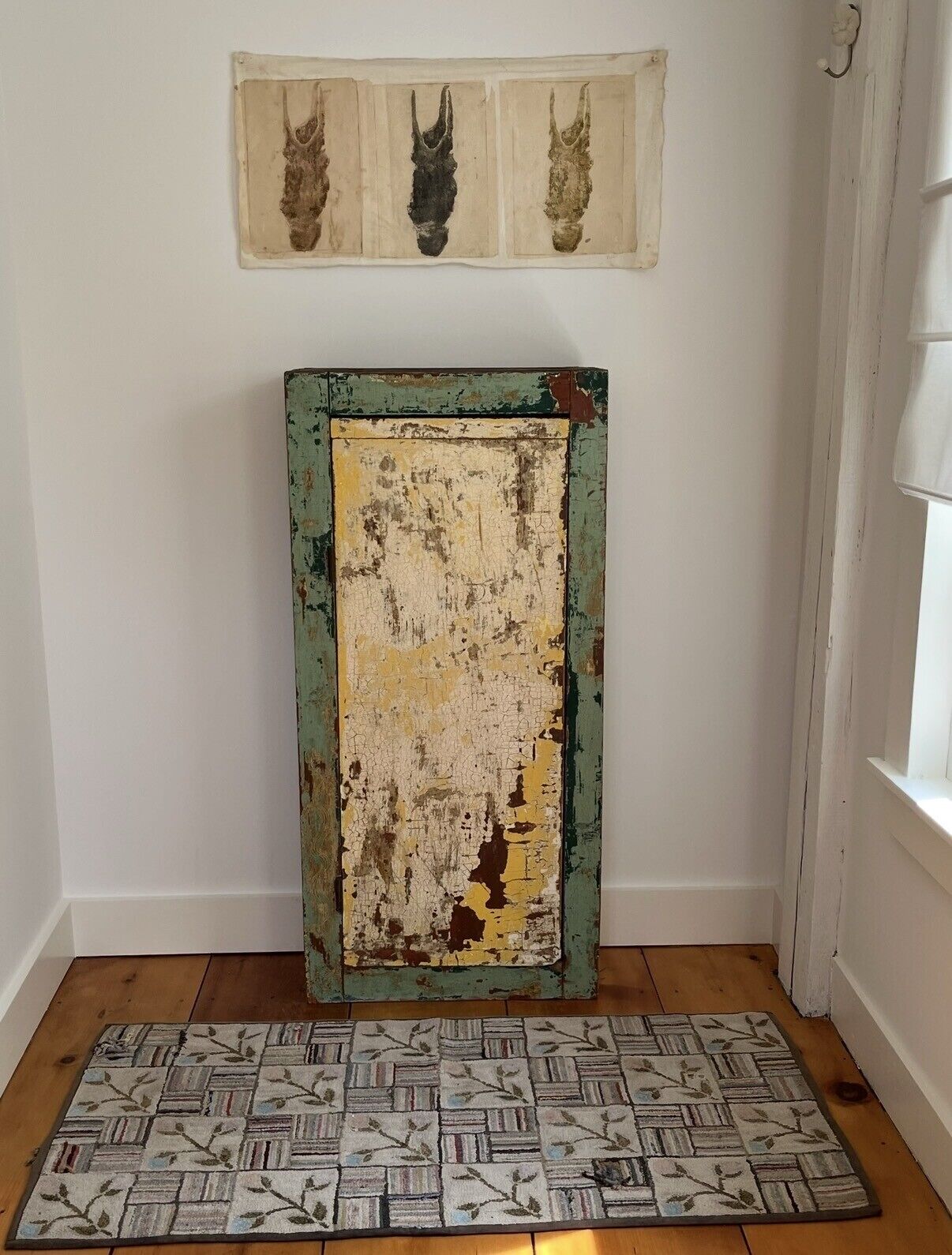 A room with a rustic, distressed wooden door, a patterned rug, and a wall-mounted artwork above the door.