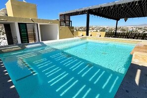 Ein Pool auf dem Dach mit klarem, blauem Wasser, einer Pergola und Blick auf die Stadtlandschaft.