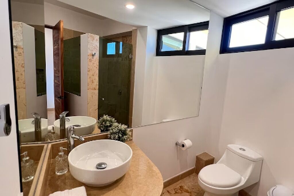 A bathroom with a large mirror, a sink, a toilet, and a shower area.