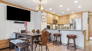 A modern kitchen with wooden cabinets, a stainless steel refrigerator, a microwave, and a flat-screen TV mounted above the counter. - Lodge Tower 578 2BR at the base of Vail Mountain (Vail)
