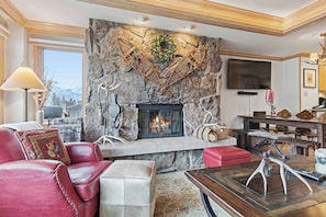 A living room with a stone fireplace, leather furniture, and a television mounted on the wall. - Lodge Tower 578 2BR at the base of Vail Mountain (Vail)