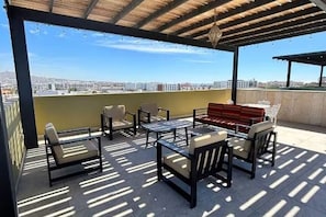 Eine Terrasse im Freien mit Sitzgelegenheiten und Blick auf die Stadt, darüber eine Pergola.