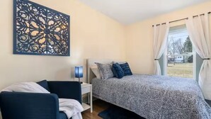 A bedroom with a bed, a chair, a nightstand, a lamp, and a decorative wall piece. - Steps to Ariel Park / Renovated 2BR Retreat (Mount Vernon)
