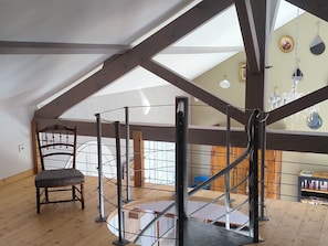 A high-ceilinged room with a wooden floor, a chair, a metal staircase, and a chandelier. - The Little House in Givry (Givry)