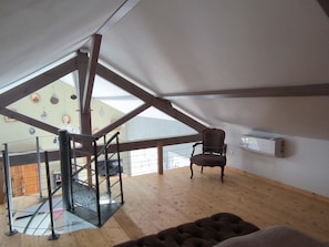 Quarto estilo loft com piso de madeira, uma cadeira, uma escada e um claraboia.
