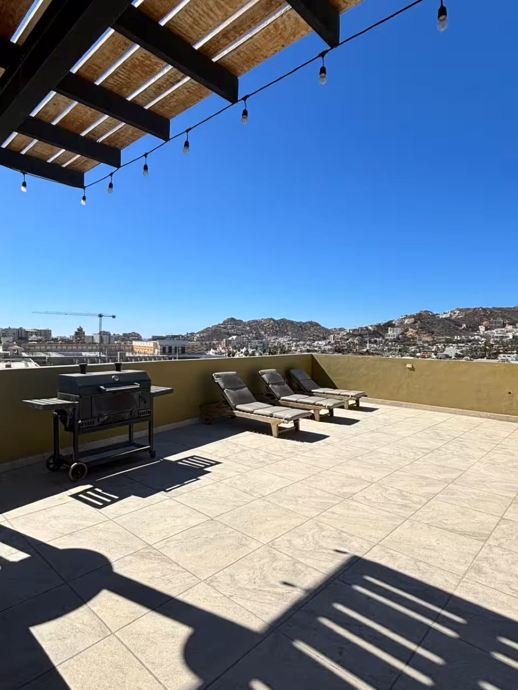 A rooftop terrace with a grill, lounge chairs, and a view of a cityscape.