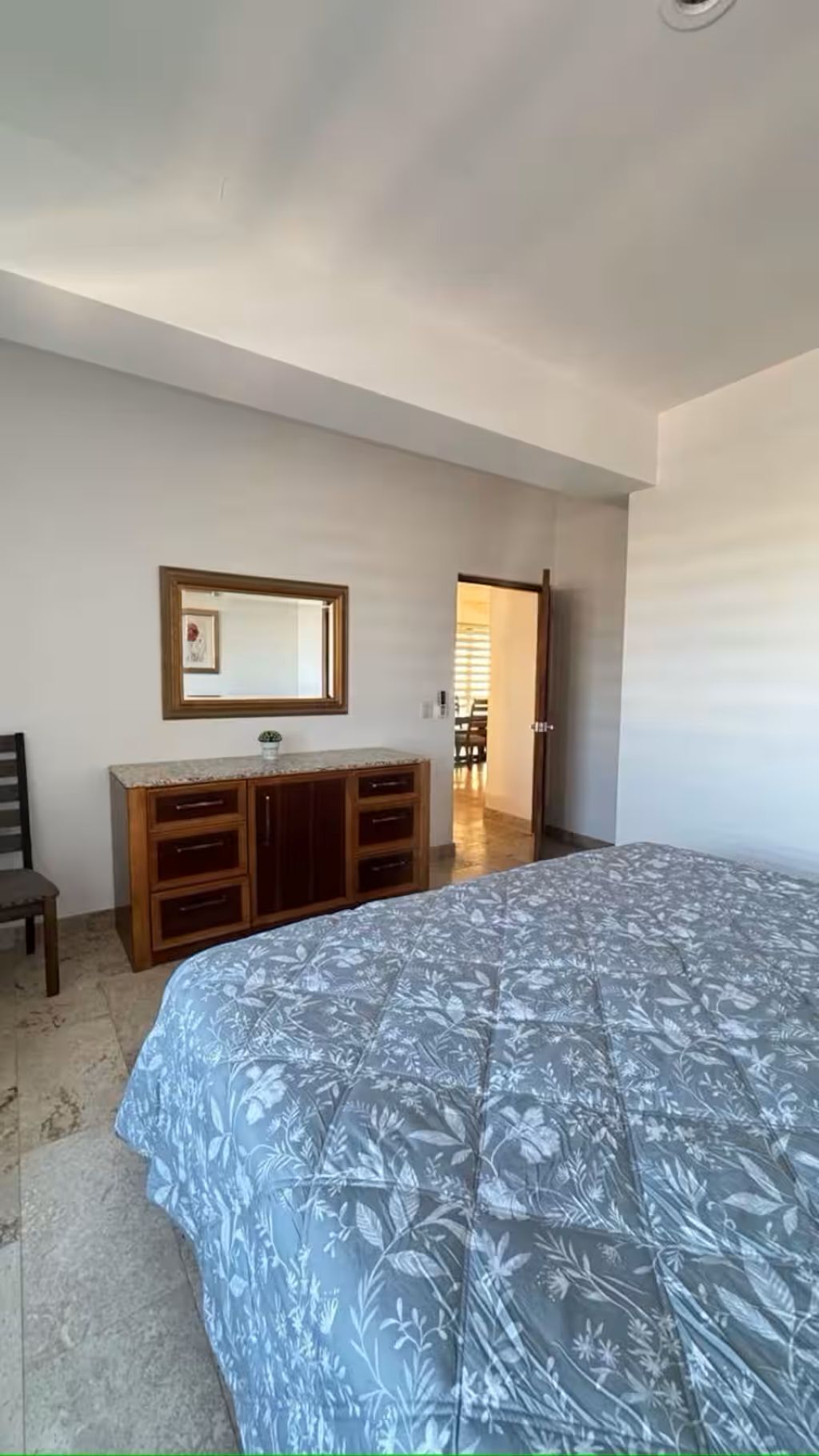 A bedroom with a bed, a wooden dresser, a mirror, and a door leading to another room.
