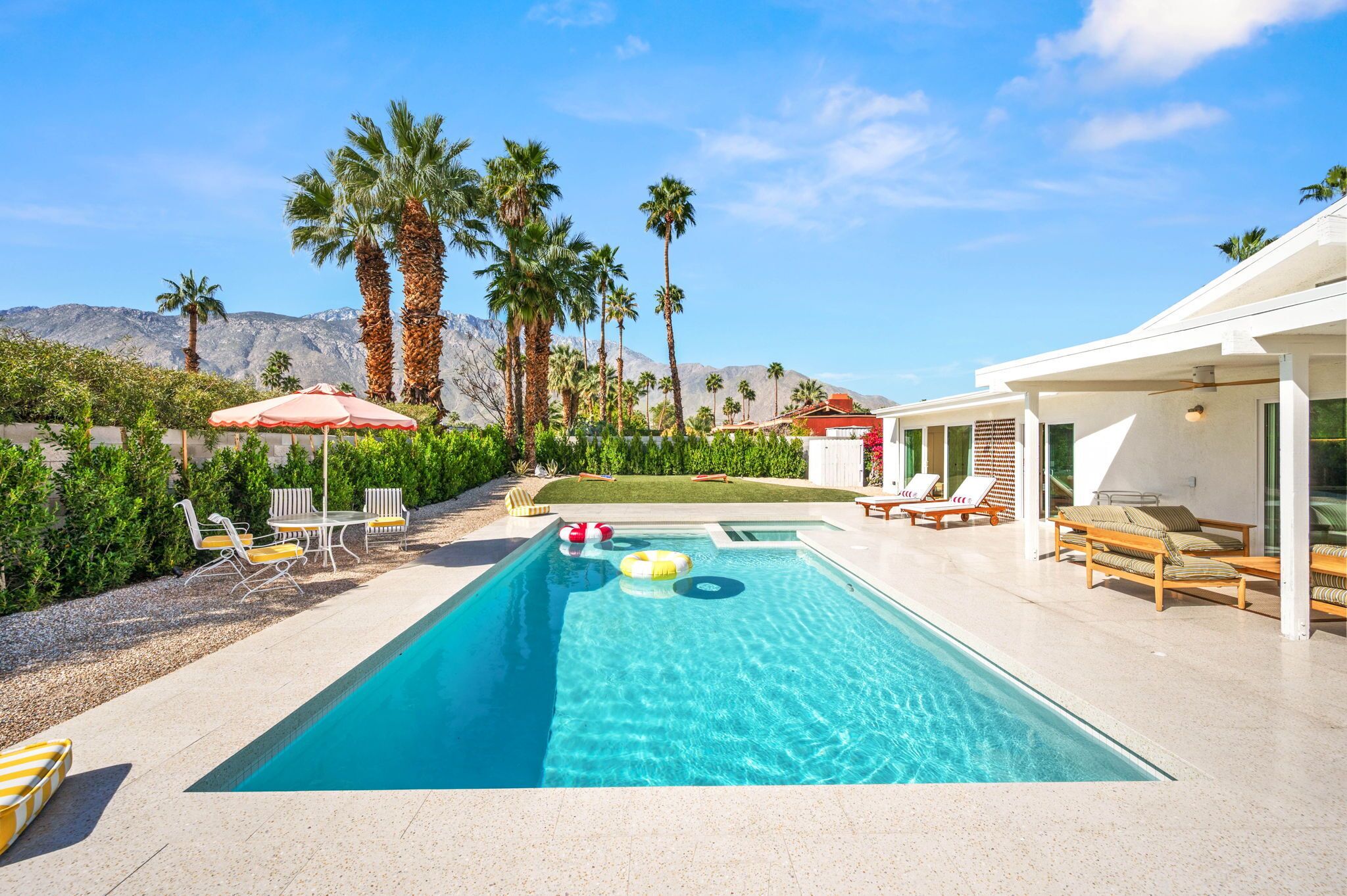 A swimming pool with lounge chairs and umbrellas, surrounded by palm trees and a mountain backdrop.