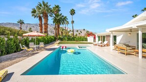 Une piscine entourée de chaises longues et de parasols, bordée de palmiers et avec une chaîne de montagnes en toile de fond.