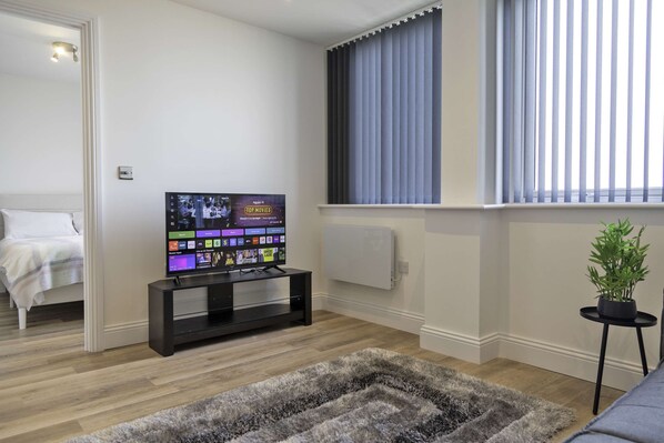 Un soggiorno moderno con una TV a schermo piatto, una tappeto shag grigio, un letto e una pianta in vaso.