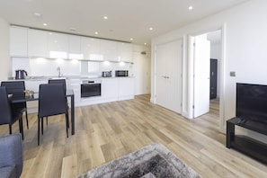A modern kitchen with white cabinets, a dining area with a table and chairs, and a living room with a TV and a sofa.