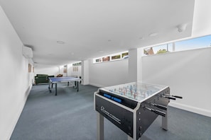 A room with a foosball table, a ping pong table, and a green sofa.