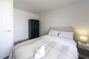Una camera d'albergo con un letto, un comodino con una lampada, un armadio e una porta.