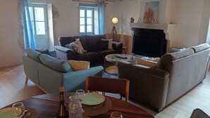 Una sala de estar con sofás, chimenea, una mesa de comedor dispuesta con platos, vasos y una botella de vino.