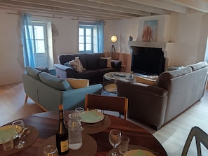 A living room with sofas, a fireplace, a dining table set with plates, glasses, and a wine bottle.