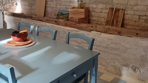 Uma área de jantar rústica, com uma parede de pedra, uma prateleira de madeira com uma garrafa e uma mesa com cadeiras.