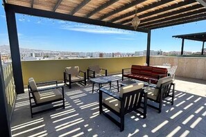 Eine Terrasse im Freien mit Sitzgelegenheiten und Blick auf die Stadt, darüber eine Pergola.