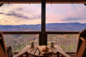 A wooden table with two white mugs and a plate of cookies, overlooking a mountainous landscape through a wire mesh window. - Pool/HotTub/GameRoom/Theater/FirePit/VIEWS - Coal Camp Lodge (Sevierville)