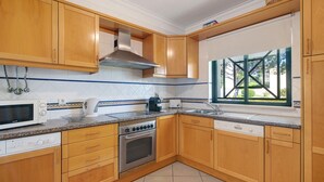 Cozinha com armários de madeira, micro-ondas, fogão e janela com vista.