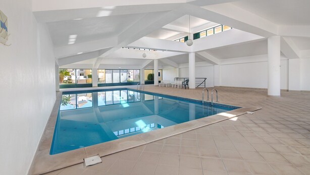 Piscina interior com chão em azulejo, teto transparente e vista para o exterior.